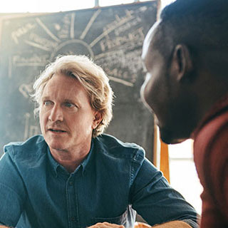 Two people having a discussion around a table with a chalkboard in the background.