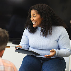 A group of five people engaged in a discussion, with a woman holding a tablet and smiling.